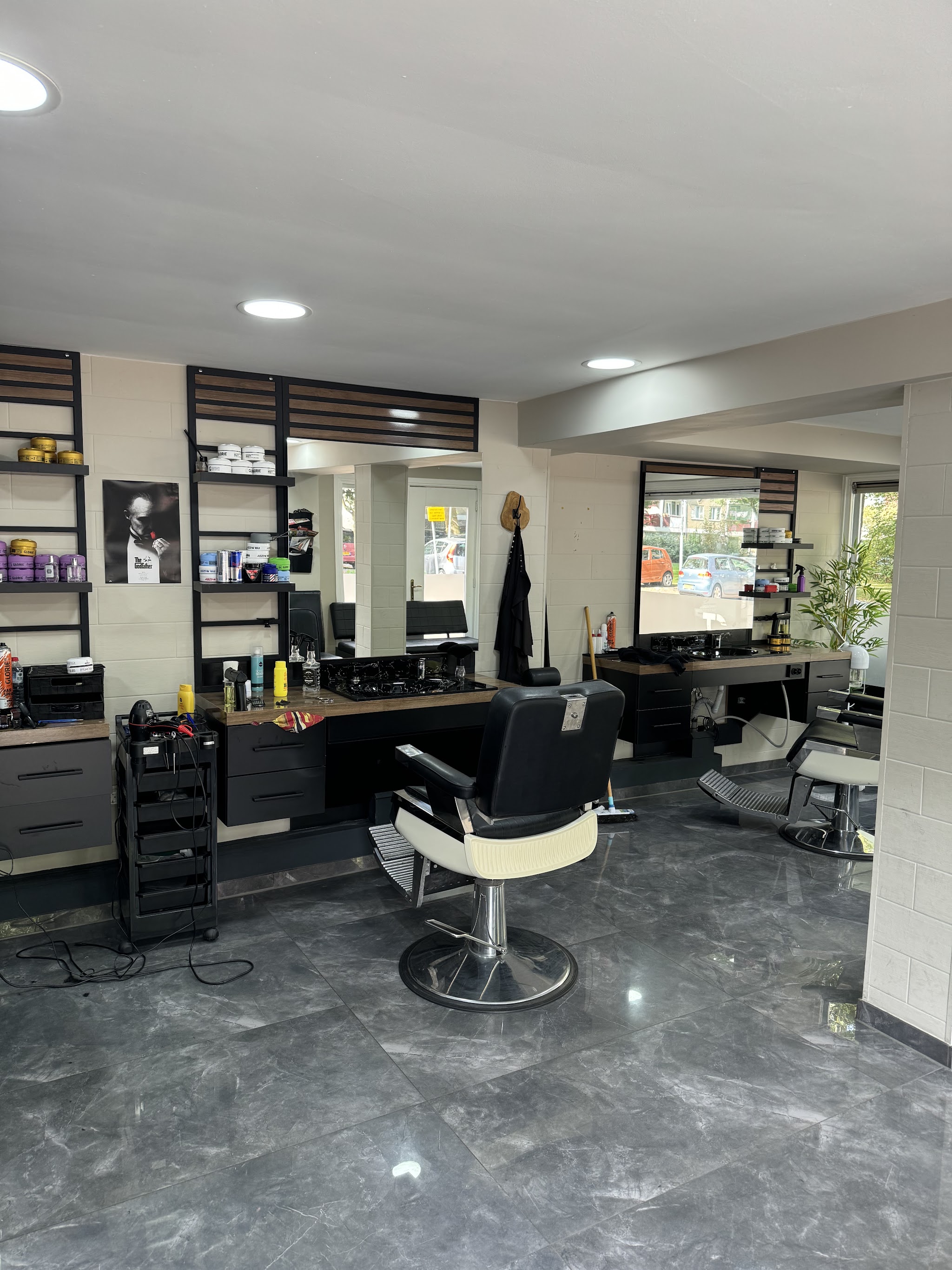 Binnen bij The Corner Barbershop: twee kappersstoelen, een wand met producten en een donkere vloer