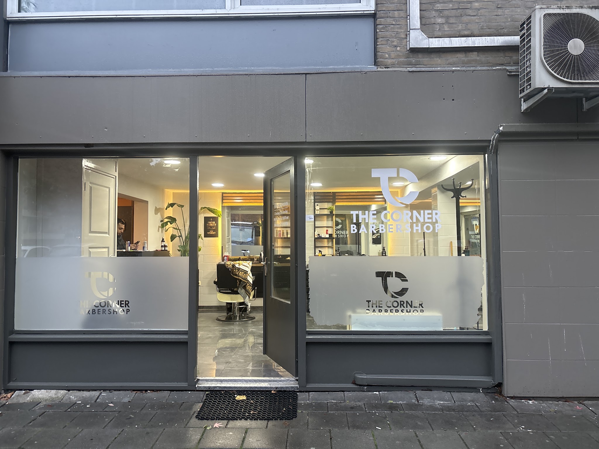 De voorgevel van The Corner Barbershop met het TC-logo op de ramen en de open deur